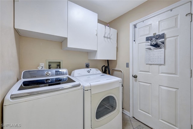 clothes washing area with washing machine and dryer, light tile patterned floors, and cabinets