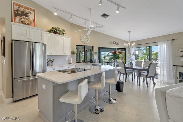 kitchen featuring a center island, lofted ceiling, white cabinets, black electric stovetop, and stainless steel refrigerator