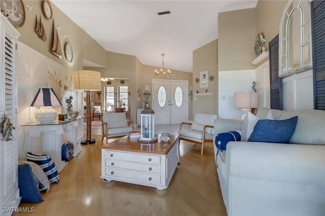 living room featuring a notable chandelier, light hardwood / wood-style floors, lofted ceiling, and french doors