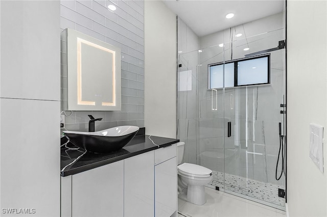 bathroom with a shower with door, vanity, tile walls, and toilet