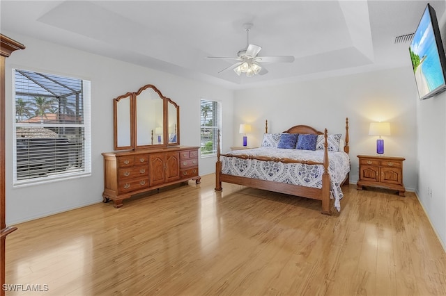 bedroom with a tray ceiling, ceiling fan, and light wood-type flooring