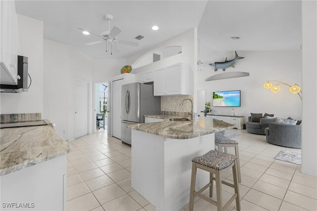 kitchen with white cabinets, appliances with stainless steel finishes, light stone counters, kitchen peninsula, and a breakfast bar area