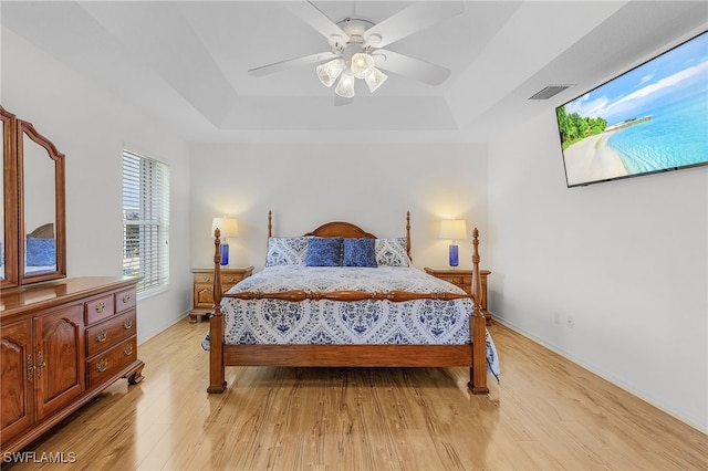 bedroom featuring ceiling fan, light hardwood / wood-style floors, and a tray ceiling