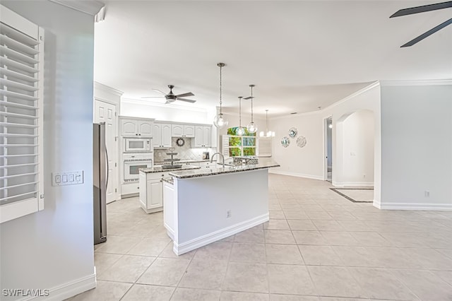 kitchen featuring dark stone counters, white appliances, a center island with sink, white cabinets, and light tile patterned flooring