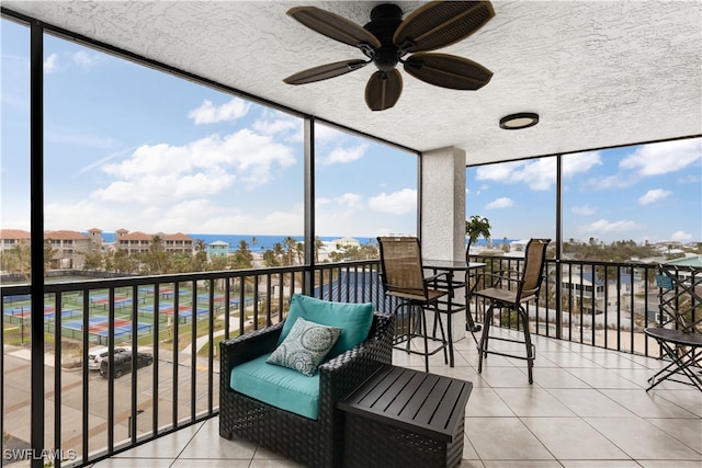 sunroom with ceiling fan and a water view