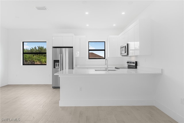 kitchen featuring kitchen peninsula, appliances with stainless steel finishes, white cabinetry, and a wealth of natural light