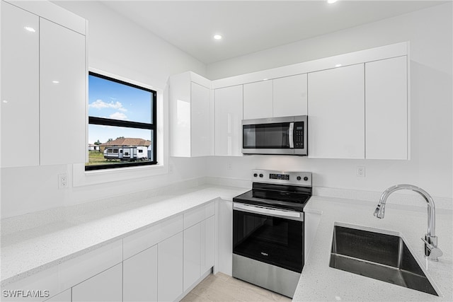 kitchen featuring white cabinetry, sink, stainless steel appliances, and light stone counters