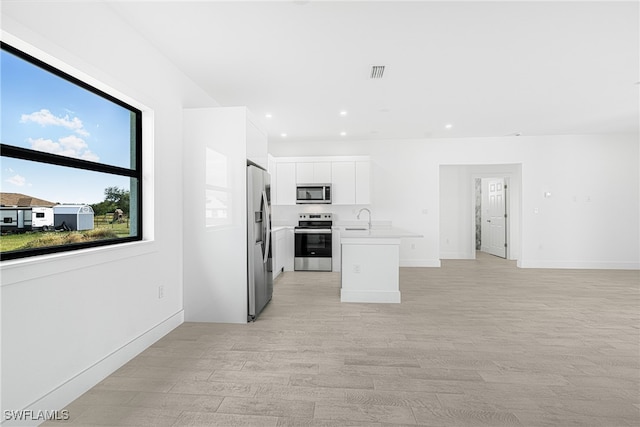 kitchen with light wood-type flooring, stainless steel appliances, white cabinetry, and an island with sink