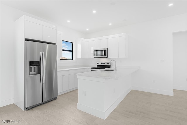 kitchen with white cabinets, sink, appliances with stainless steel finishes, light hardwood / wood-style floors, and kitchen peninsula