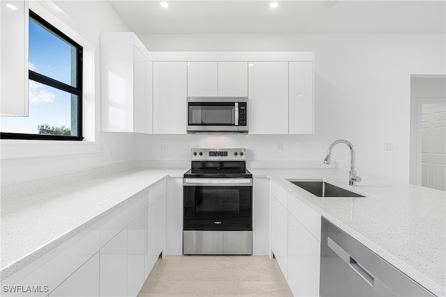 kitchen with appliances with stainless steel finishes, light stone counters, sink, light hardwood / wood-style floors, and white cabinetry