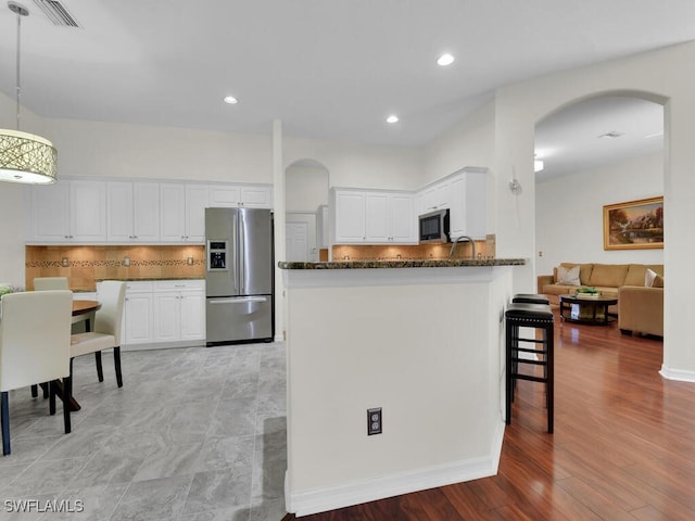 kitchen with pendant lighting, white cabinets, decorative backsplash, light wood-type flooring, and stainless steel appliances