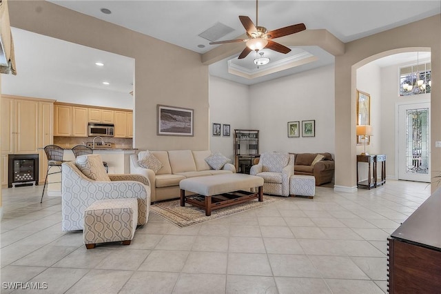 living room with light tile patterned floors, ceiling fan with notable chandelier, crown molding, and a high ceiling