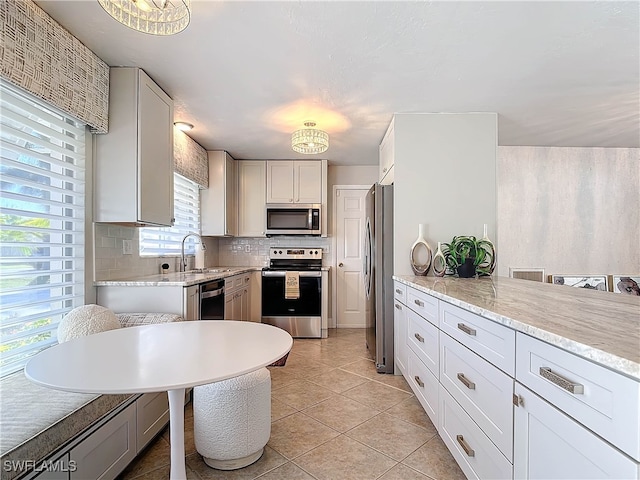 kitchen with white cabinets, decorative backsplash, light stone countertops, appliances with stainless steel finishes, and light tile patterned flooring