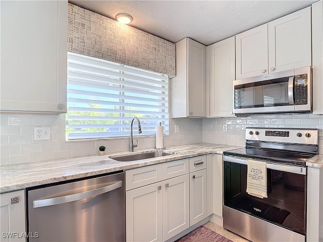 kitchen featuring decorative backsplash, appliances with stainless steel finishes, light stone countertops, sink, and white cabinets