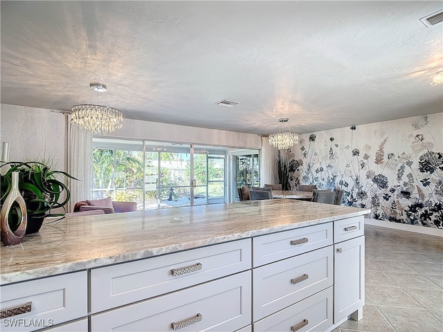 kitchen with light stone countertops, white cabinets, decorative light fixtures, and a notable chandelier