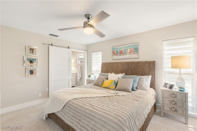 bedroom with ceiling fan, a barn door, and light carpet