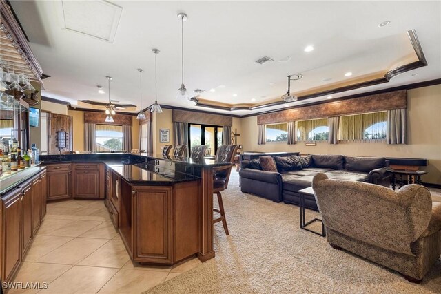 kitchen featuring pendant lighting, ceiling fan, ornamental molding, a tray ceiling, and a breakfast bar area