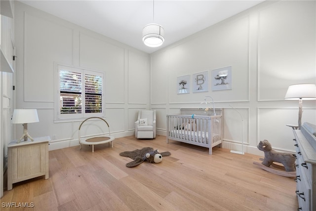 bedroom featuring light wood-type flooring and a nursery area