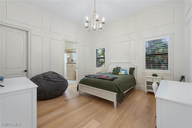 bedroom featuring ensuite bathroom, light wood-type flooring, and an inviting chandelier