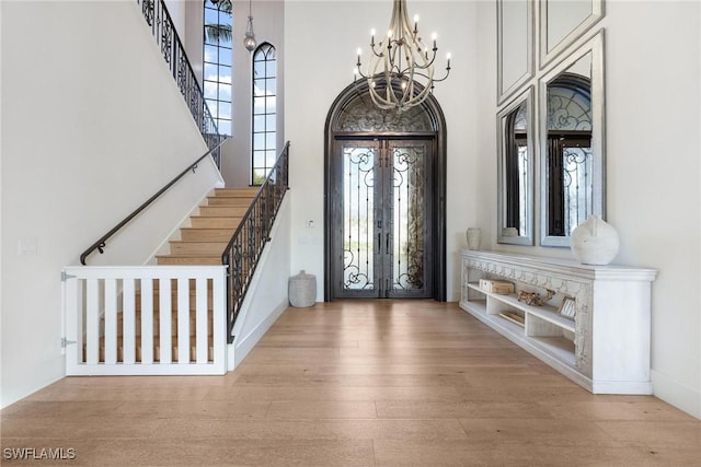 foyer with a notable chandelier, light hardwood / wood-style floors, a high ceiling, and french doors