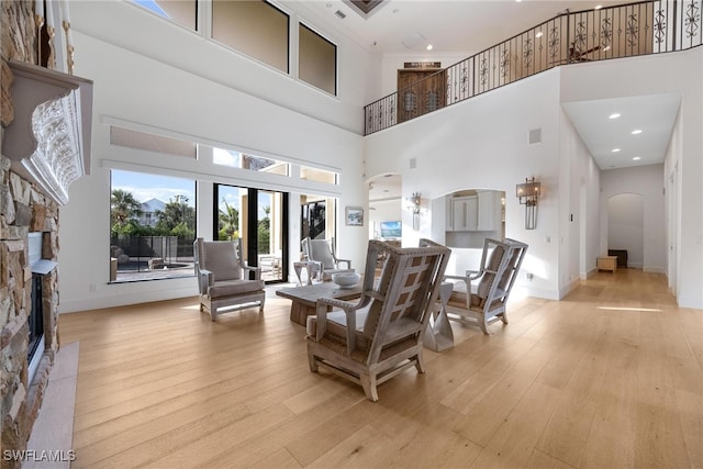 living room featuring a stone fireplace, a high ceiling, and light hardwood / wood-style flooring