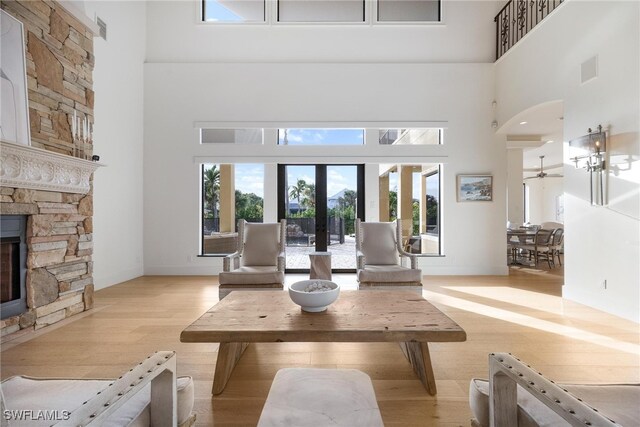 living room featuring ceiling fan, french doors, a high ceiling, light hardwood / wood-style flooring, and a fireplace