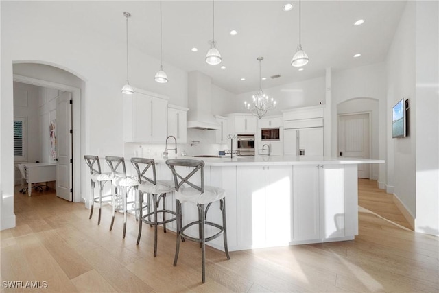 kitchen with stainless steel oven, built in fridge, decorative light fixtures, white cabinets, and custom range hood