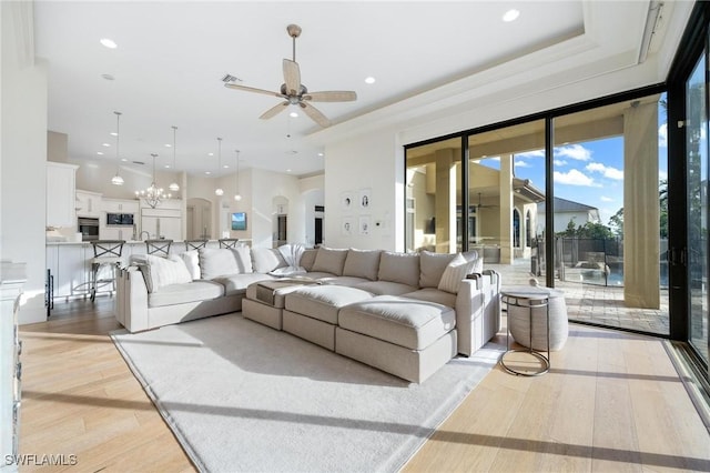 living room featuring ceiling fan with notable chandelier and light wood-type flooring