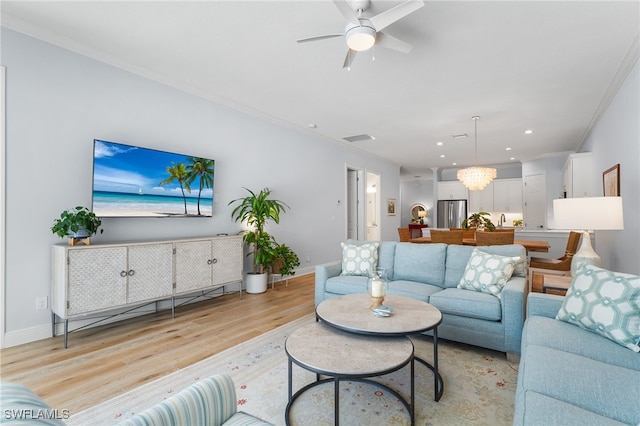 living room with ceiling fan with notable chandelier, light wood-type flooring, and crown molding