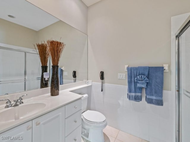 bathroom with toilet, a shower with door, tile patterned floors, vanity, and tile walls