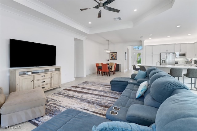 living room with a tray ceiling, ceiling fan, sink, and ornamental molding