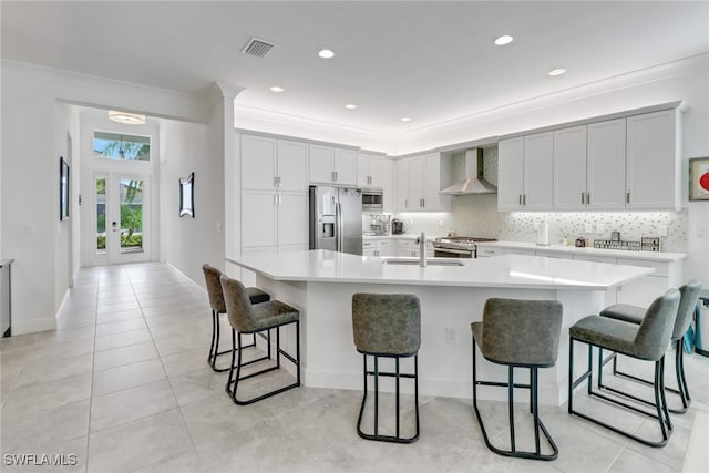 kitchen with a kitchen breakfast bar, a large island with sink, stainless steel appliances, and wall chimney range hood