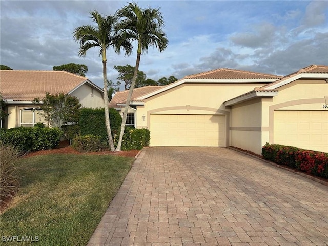 mediterranean / spanish-style house featuring stucco siding, a tile roof, an attached garage, decorative driveway, and a front yard