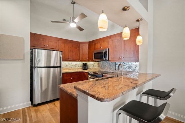 kitchen with light hardwood / wood-style floors, kitchen peninsula, stainless steel appliances, and tasteful backsplash