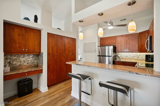 kitchen with a high ceiling, hanging light fixtures, light hardwood / wood-style floors, kitchen peninsula, and stainless steel appliances