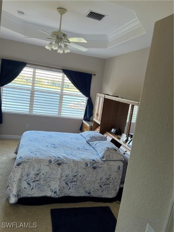 carpeted bedroom featuring ceiling fan, ornamental molding, and a tray ceiling