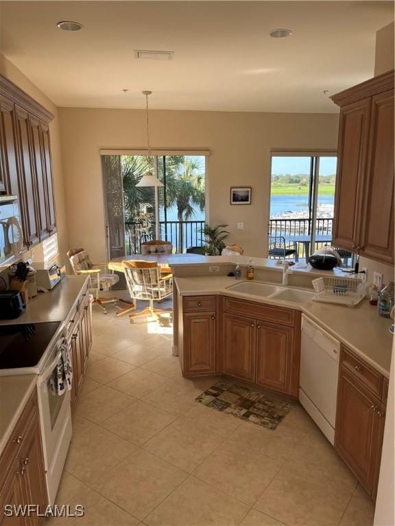 kitchen with white appliances, sink, light tile patterned floors, a water view, and hanging light fixtures