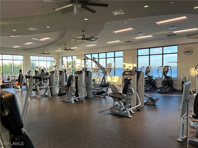 workout area with a wealth of natural light, a drop ceiling, a water view, and ceiling fan