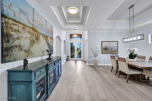 foyer with an inviting chandelier, french doors, crown molding, light wood-type flooring, and a tray ceiling