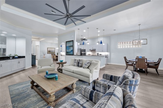 living room with light wood-type flooring, a tray ceiling, and crown molding