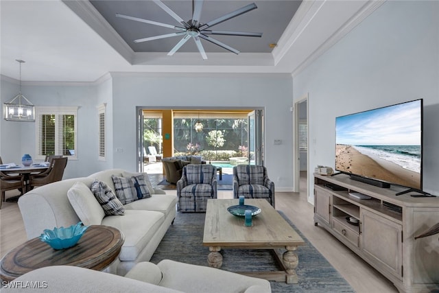 living room with ceiling fan with notable chandelier, light hardwood / wood-style floors, ornamental molding, and a tray ceiling