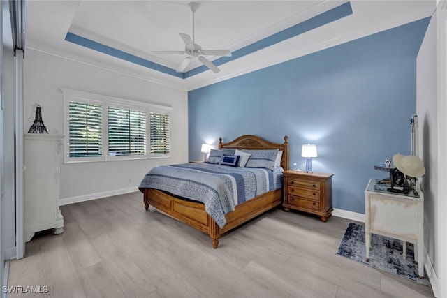 bedroom with ceiling fan, ornamental molding, a tray ceiling, and light hardwood / wood-style flooring