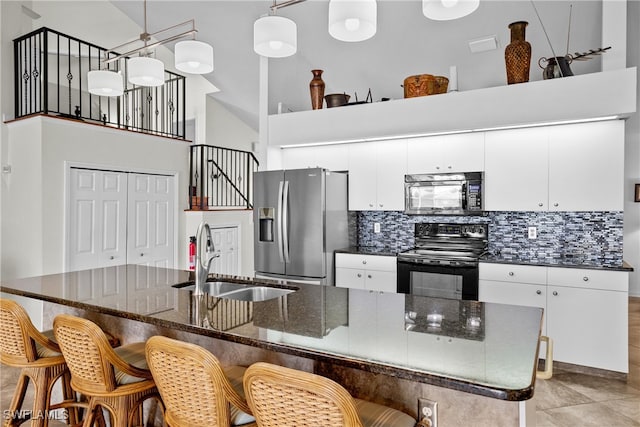 kitchen with sink, black appliances, a center island with sink, a high ceiling, and hanging light fixtures