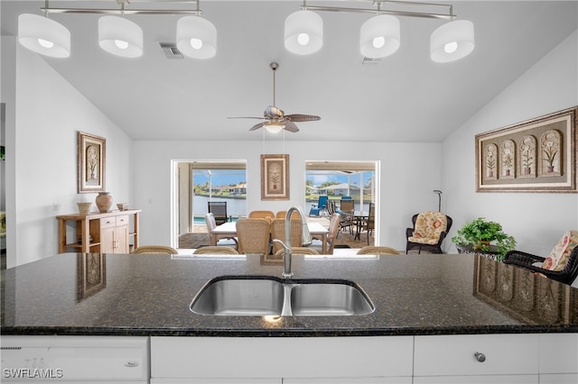 kitchen featuring pendant lighting, dark stone counters, white cabinets, sink, and vaulted ceiling