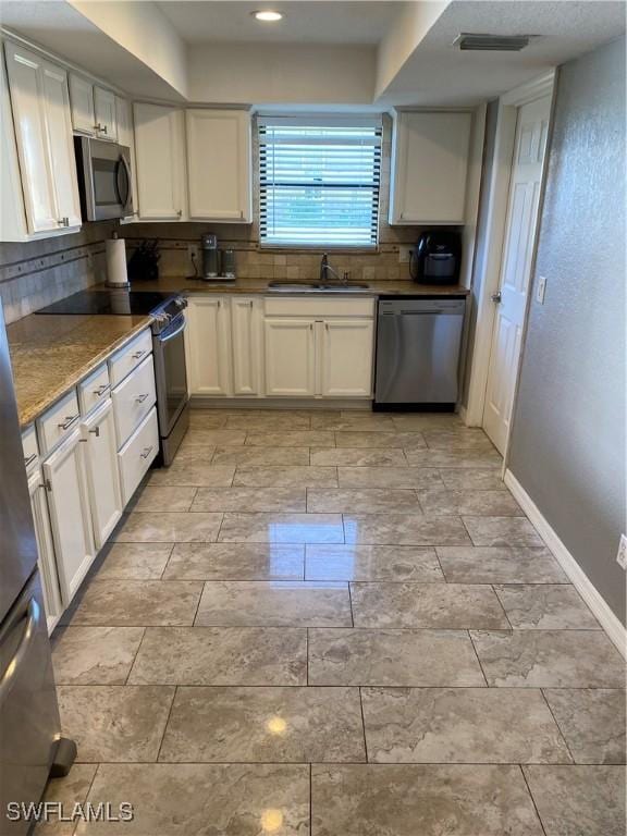 kitchen featuring backsplash, stainless steel appliances, sink, dark stone countertops, and white cabinets