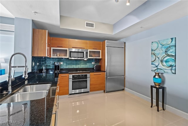 kitchen featuring backsplash, sink, dark stone countertops, light tile patterned floors, and stainless steel appliances