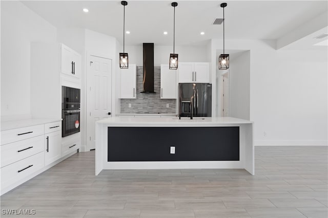 kitchen featuring white cabinetry, wall chimney range hood, pendant lighting, a center island with sink, and black appliances