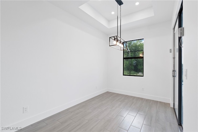 unfurnished dining area with light hardwood / wood-style floors and a raised ceiling