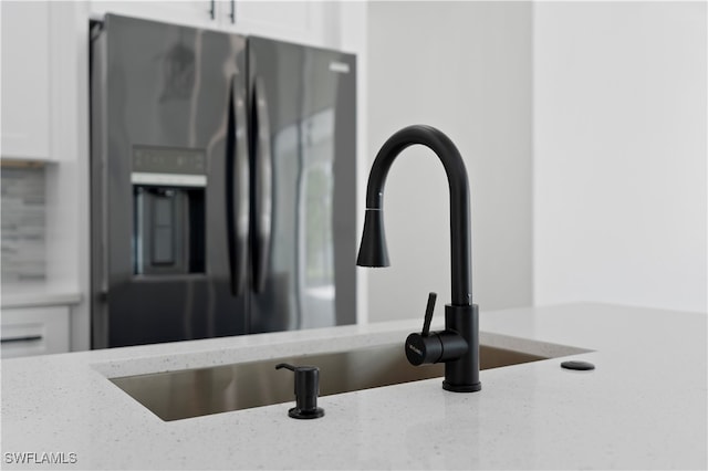 details featuring stainless steel fridge, light stone countertops, and white cabinetry