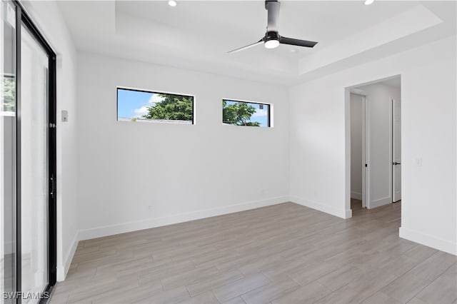 empty room with ceiling fan, light hardwood / wood-style floors, and a tray ceiling